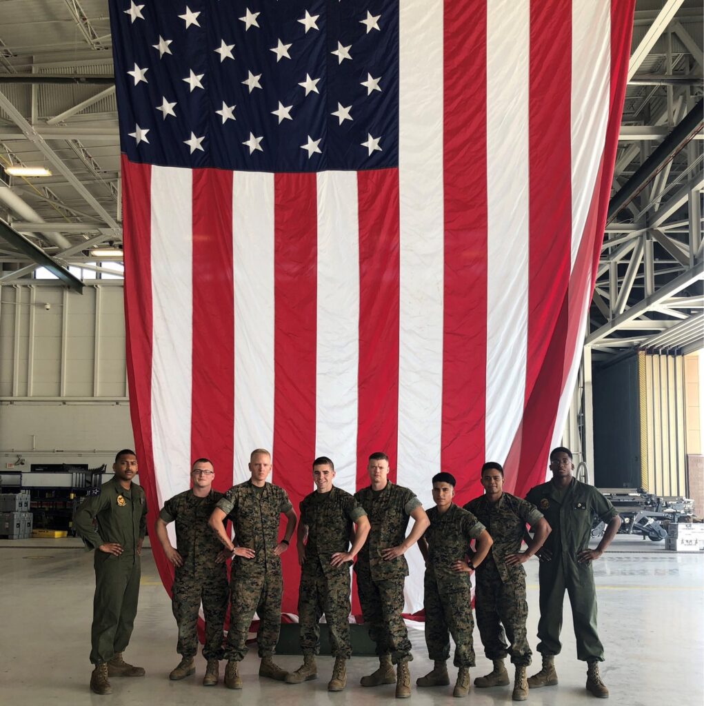 Maintainers from VMFA-211 squadron standing in front of a giant U.S Flag